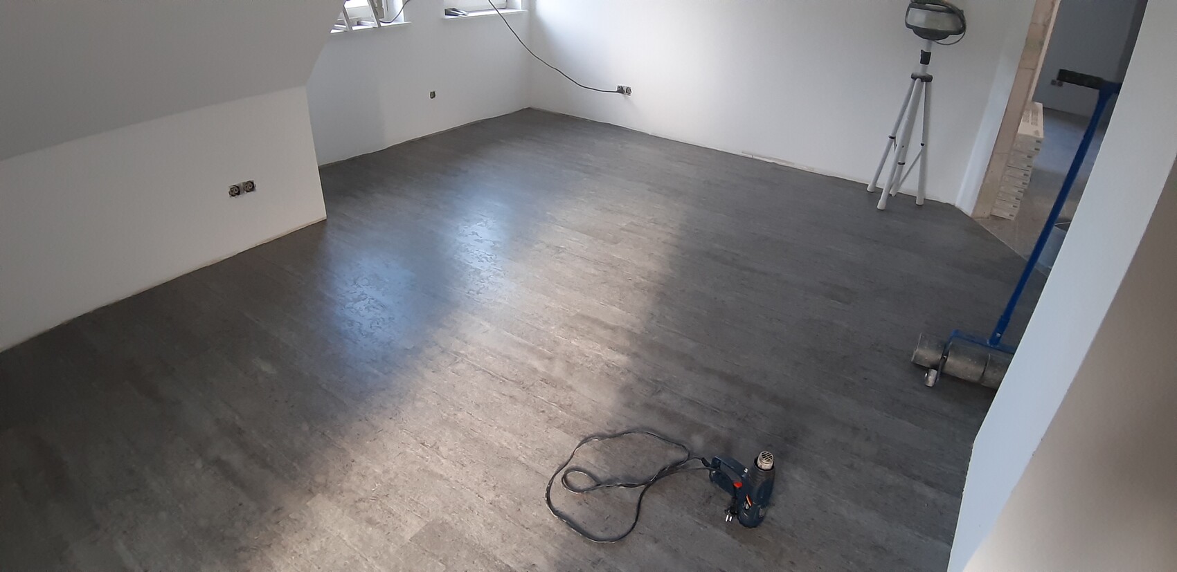 Leerer Renovierungsraum mit dunklem Boden; Bohrmaschine, Stativ mit Laser und Kabel.