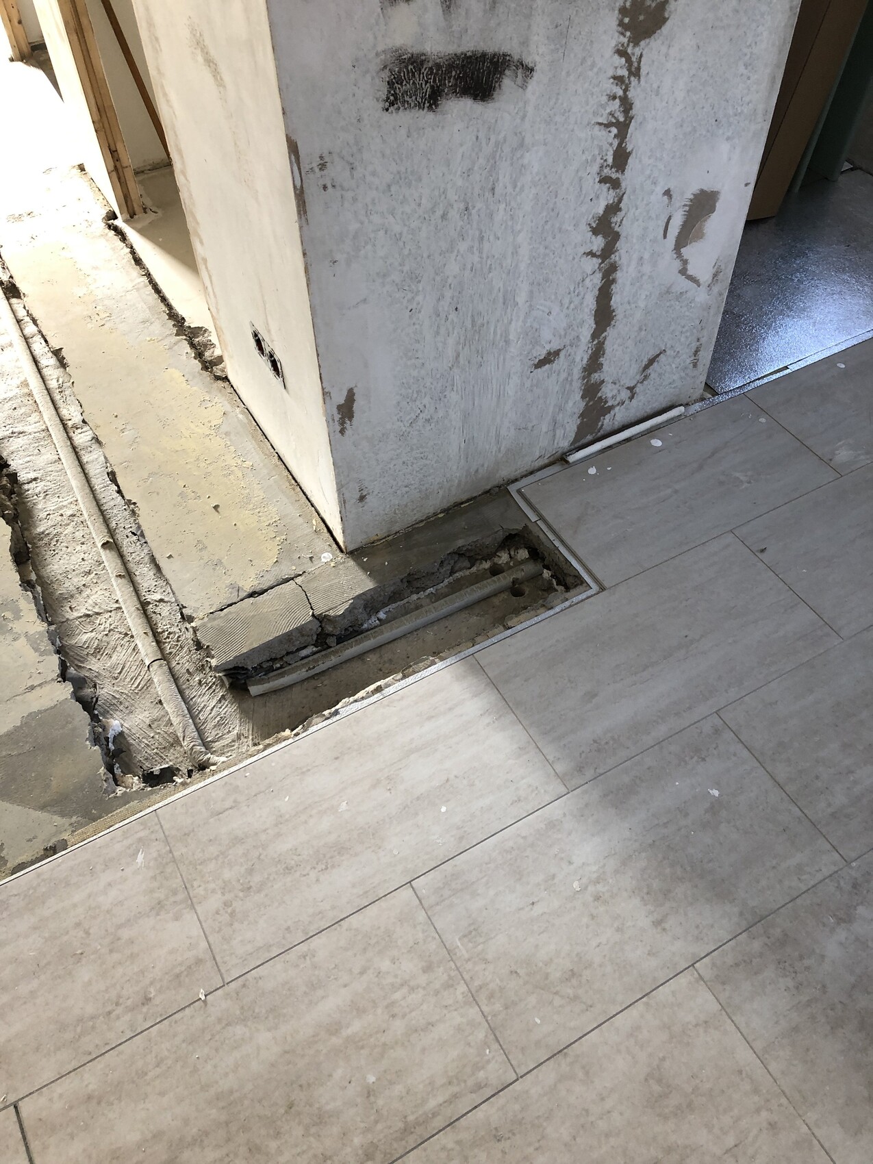 Baustelle: offener Bodenkanal neben verputztem Betonpfeiler, unvollständiger Bodenbelag.