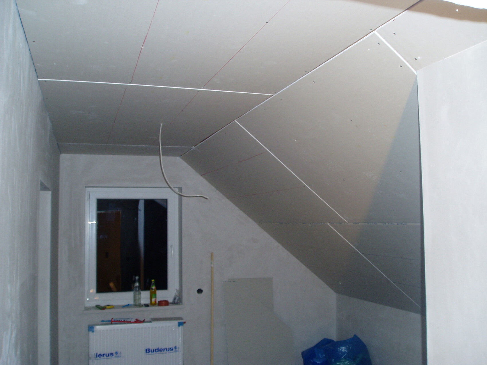 Unfertiges Innenausbauzimmer mit Trockenbauwänden, schräger Decke und Kabeln.