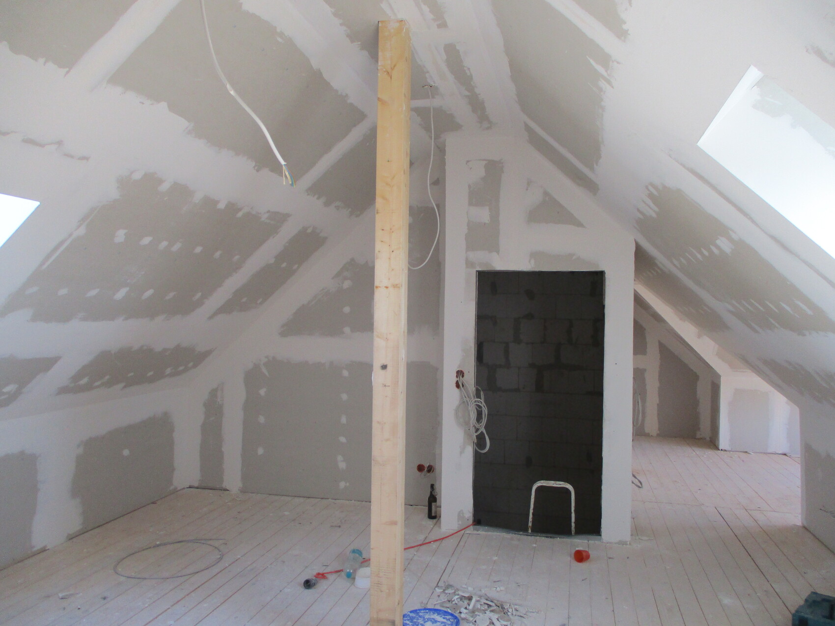 Dachboden im Rohbau: gespachtelte Wände, zentrale Holzstütze, offener Durchgang, Kabel.