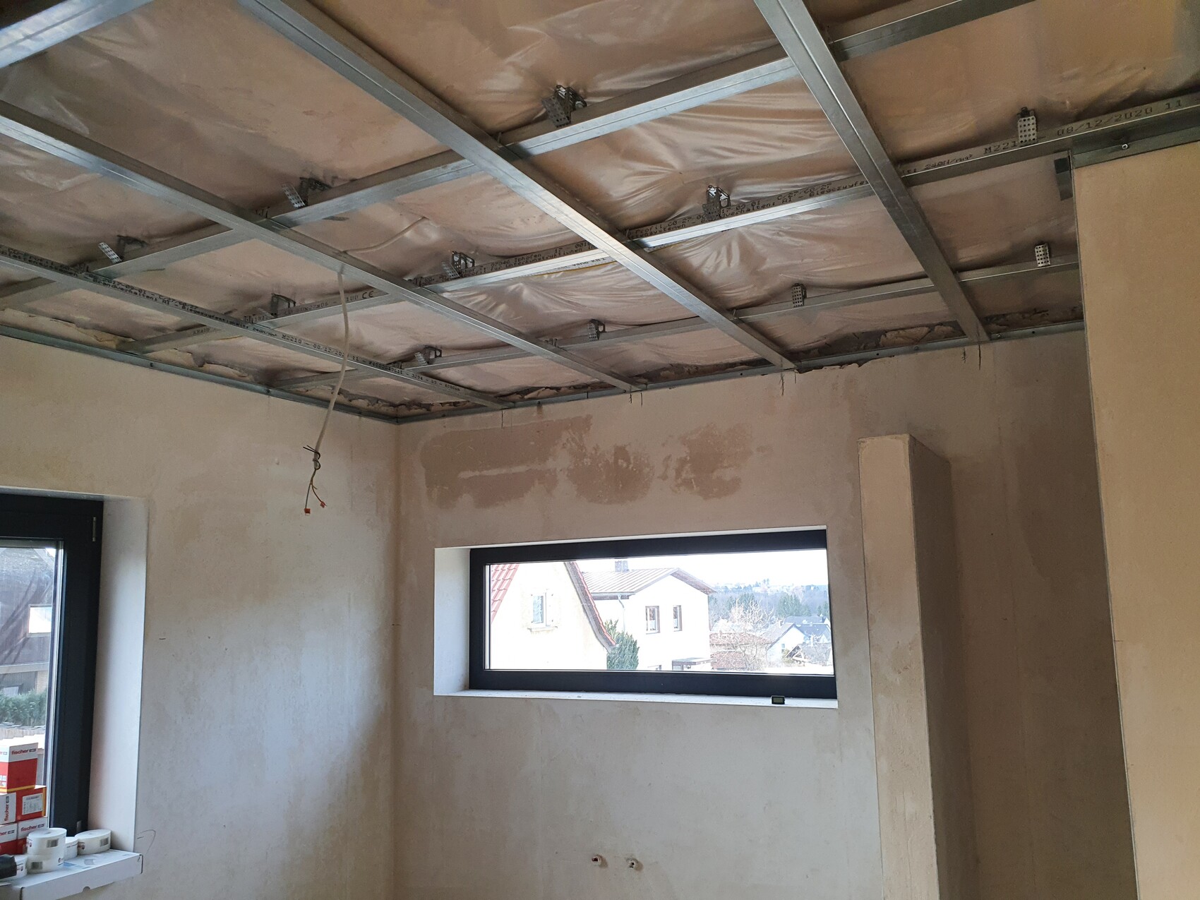 Unbearbeiteter Innenraum eines Bauprojekts mit Metall-Deckenrahmen, Dämmung und freiliegendem Kabel.