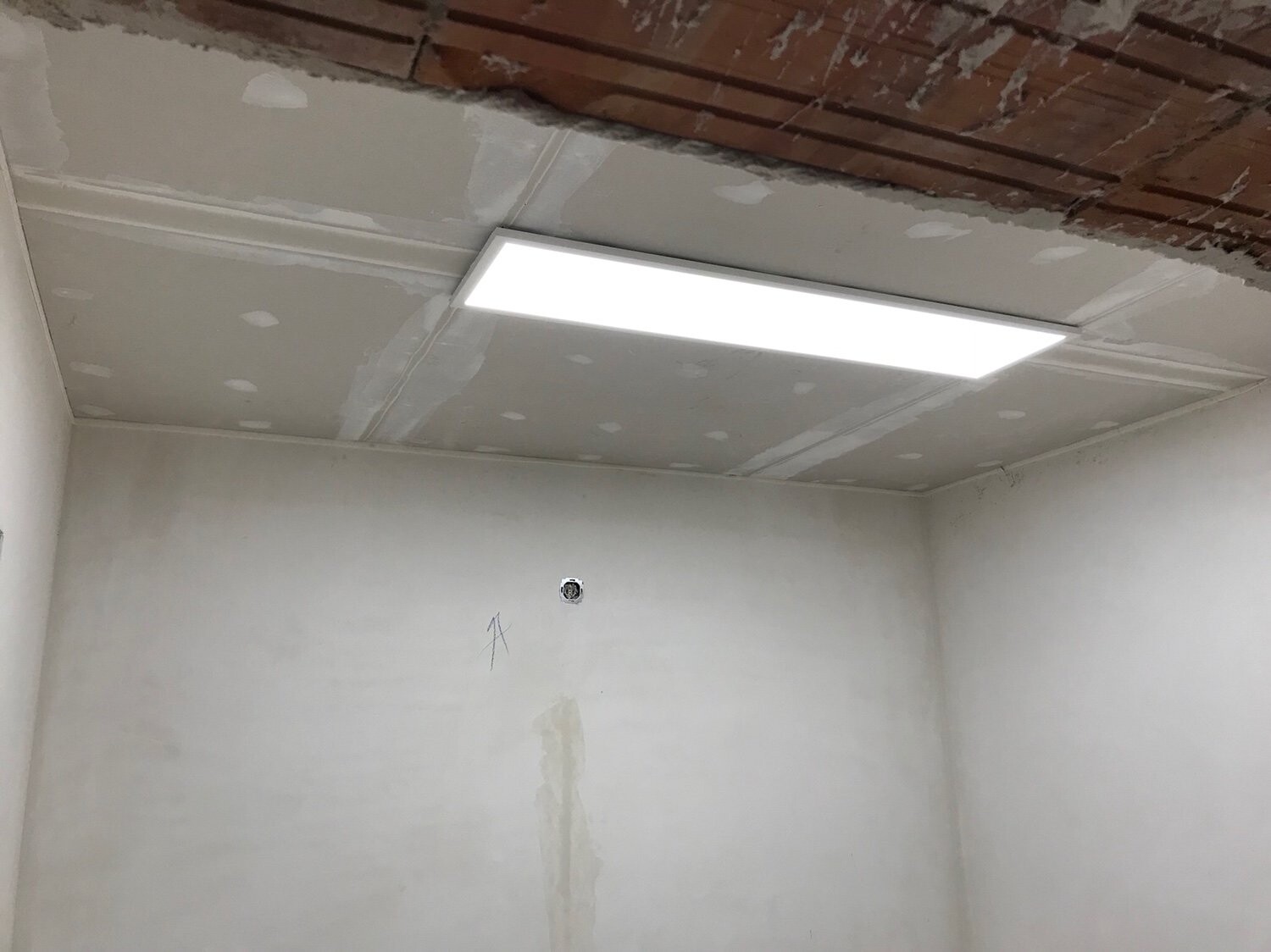 Renovierungsraum mit LED-Deckenpanel, ungeputzter Decke und Wandöffnung.