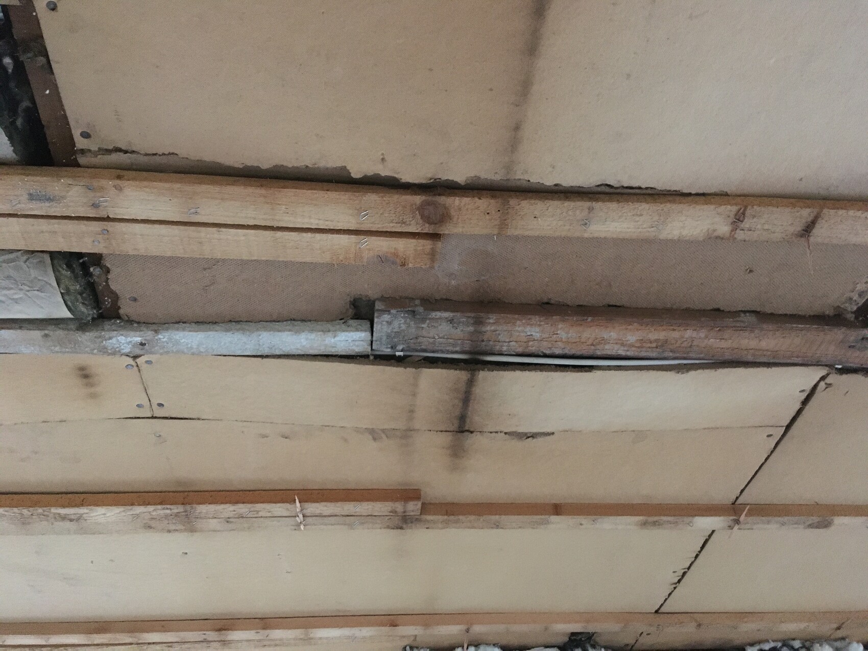 Unverputzte Decke mit Holzbalken, Brettern und Feuchtigkeitsspuren.