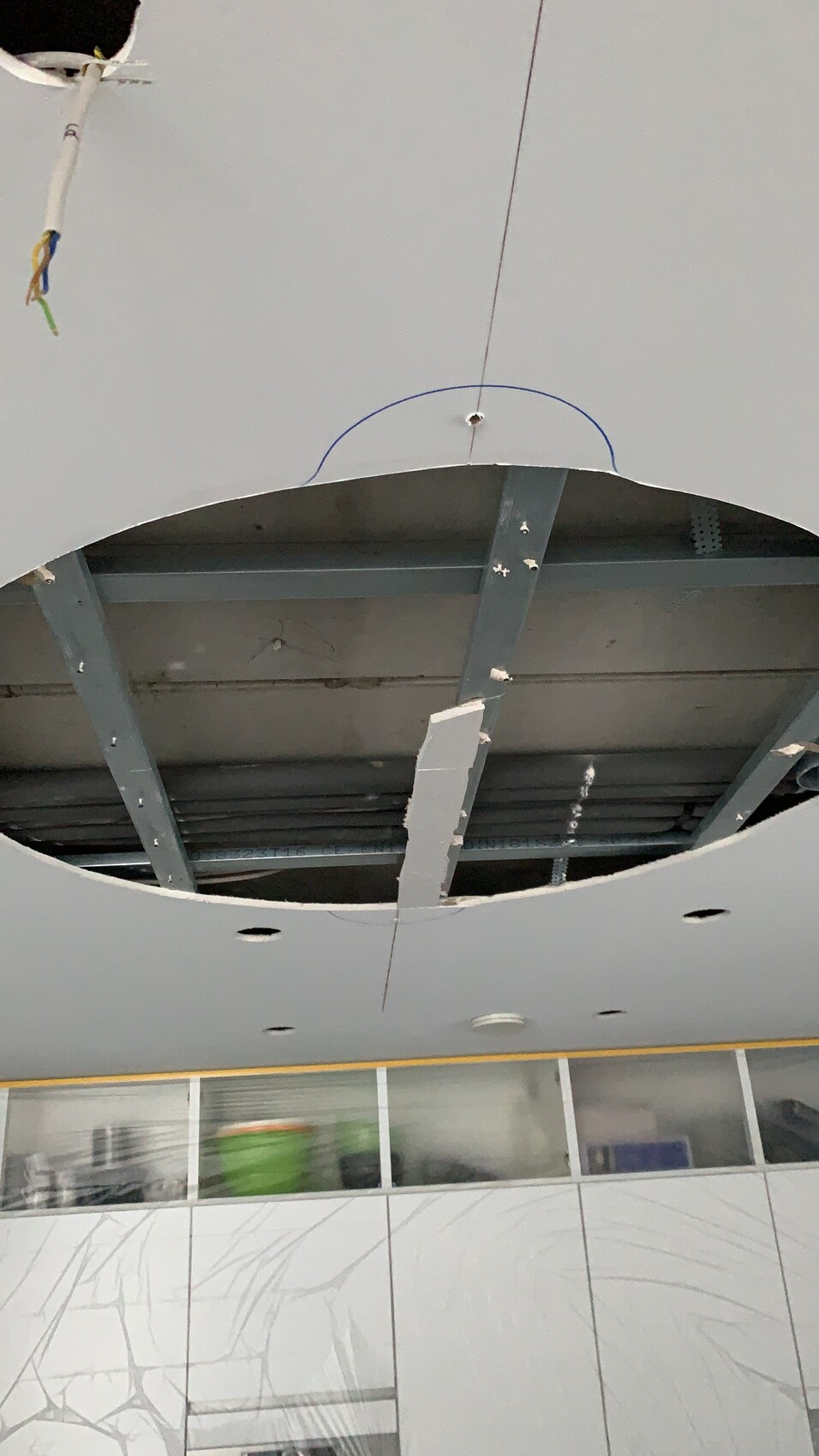 Offene Decke mit kreisrunder Aussparung, freigelegten Stahlträgern und hängenden Kabeln.