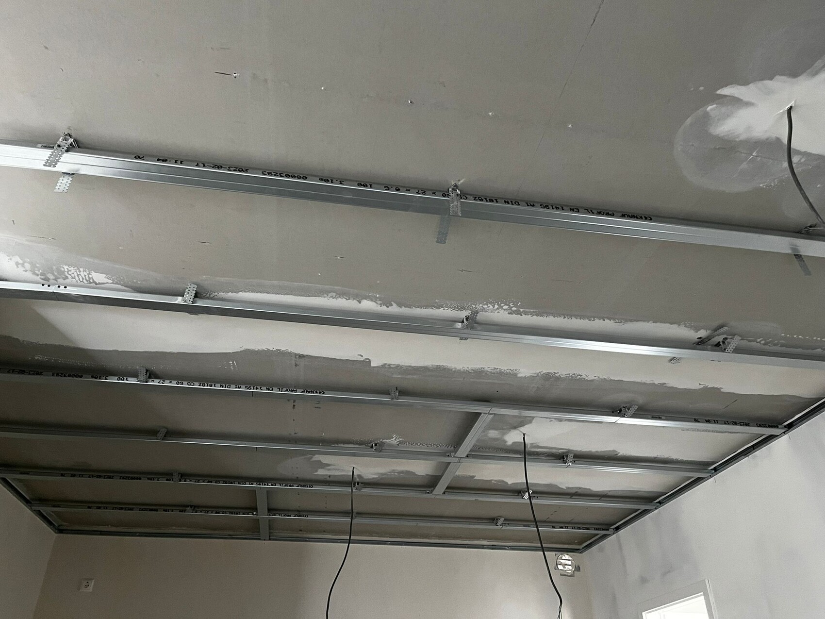 Offene Decke im Bauzustand mit Metallprofilen, Aufhängungen, Kabeln und Putzresten.