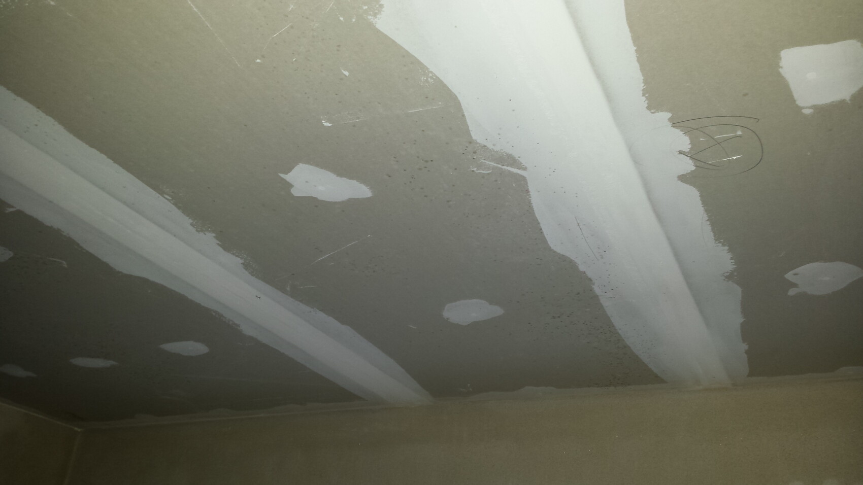 Unfertig verputzte Decke mit weißen Spachtelmasse-Flecken und Kreismarkierungen.