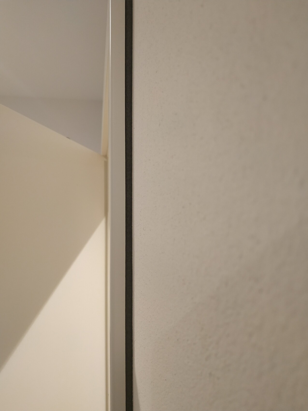 Nahaufnahme einer Türrahmenkante links neben grauer Wand, mittig sichtbare Kante
