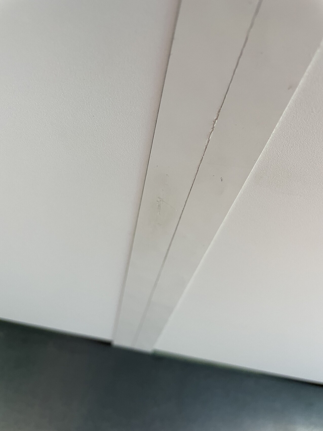 Nahaufnahme weißer Paneele mit zwei parallelen Leisten; darunter dunkler Untergrund sichtbar.