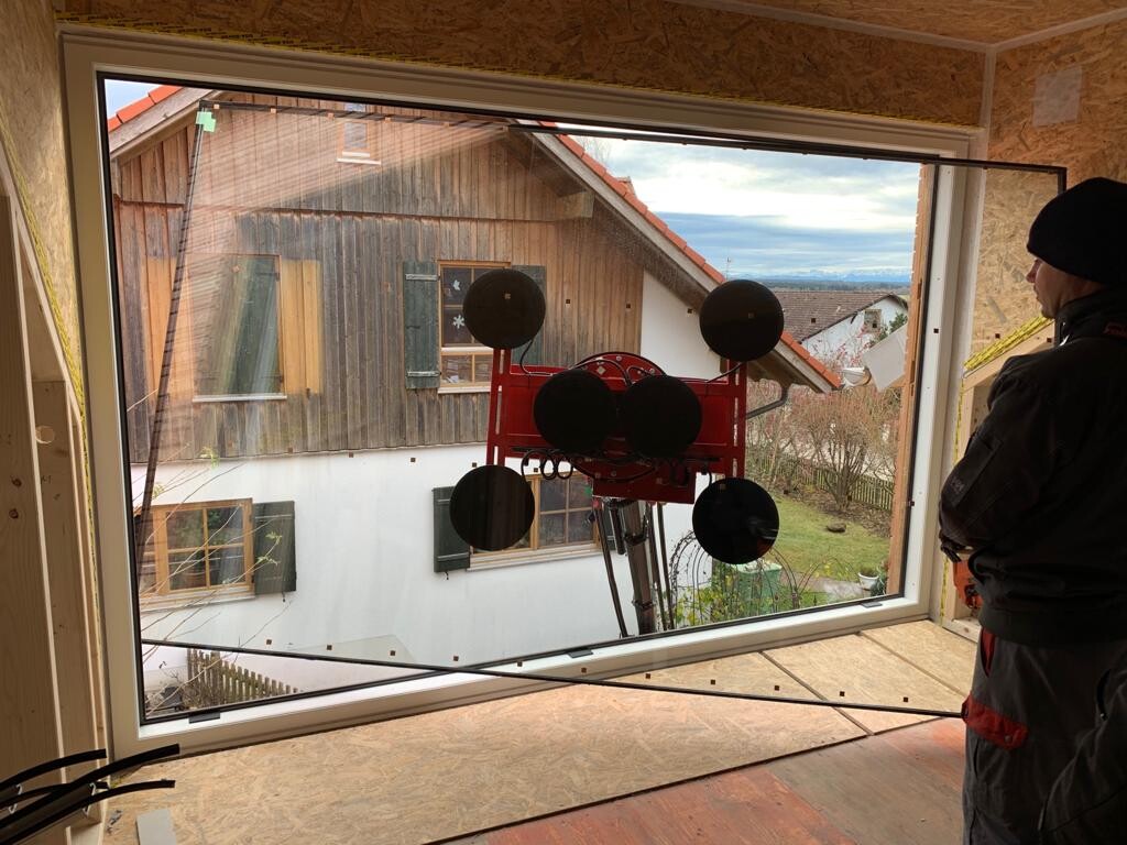 Bauarbeiter rechts neben großem Fenster; roter Glasheber mit Saugkissen, Blick nach draußen.