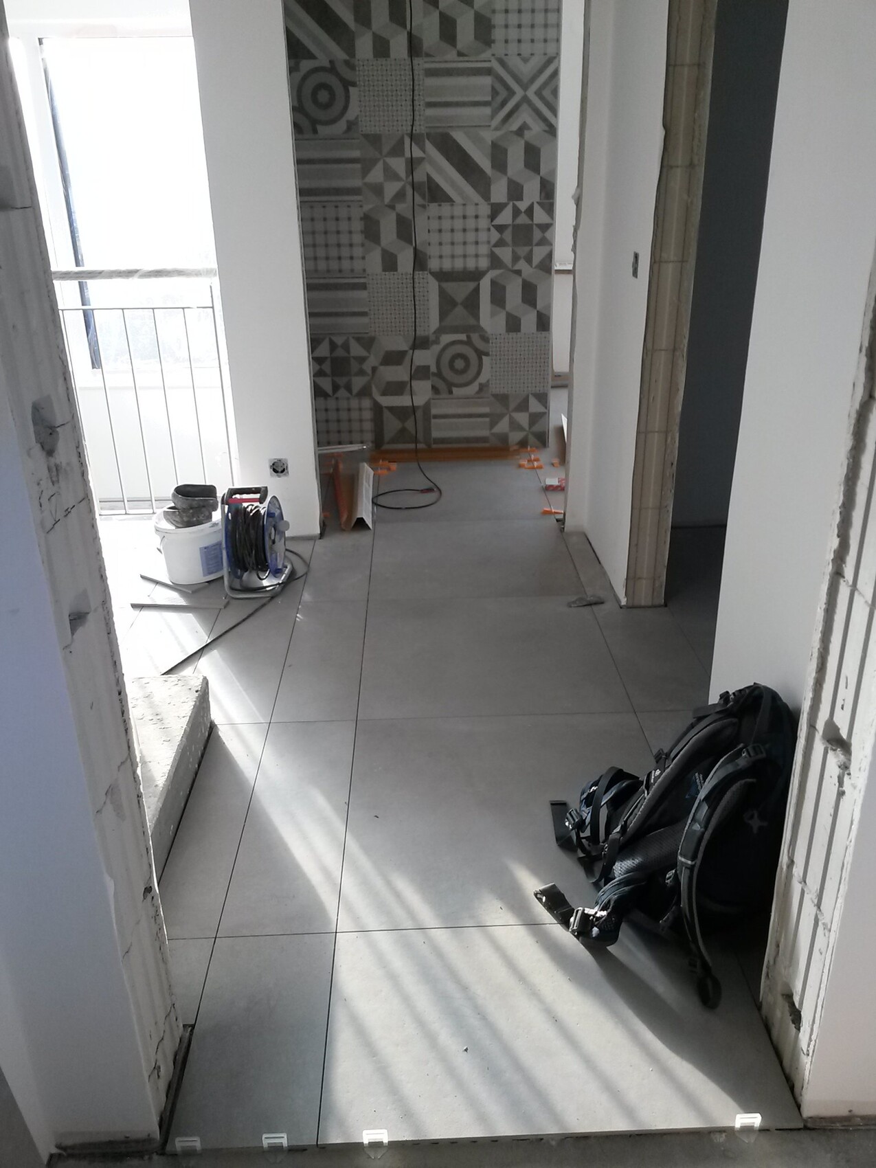 Bauflur mit grauen Bodenfliesen, gemusterten Wandfliesen, Kabelrolle und Rucksack.