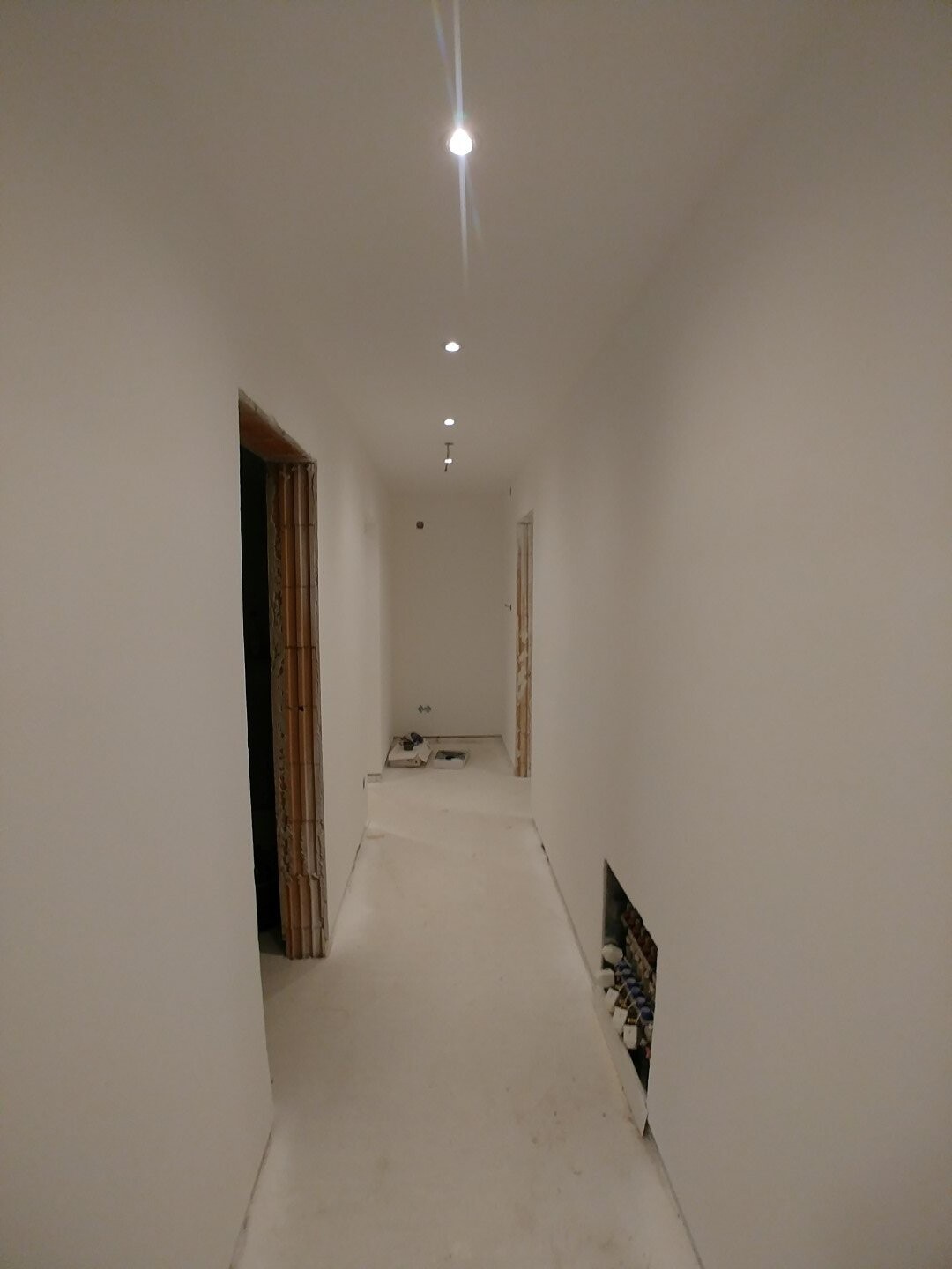 Langer heller Flur im Innenausbau mit Deckenlampen und offenen Tuerrrahmen.