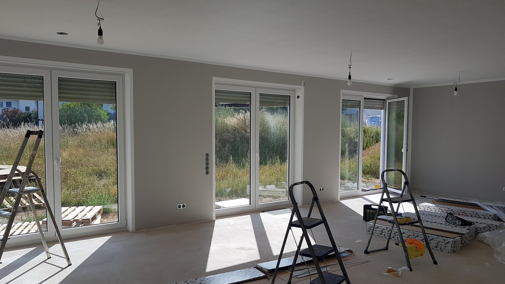 Unfertiger Wohnraum mit grossen Fensterfronten, Leitern und Baumaterialien.