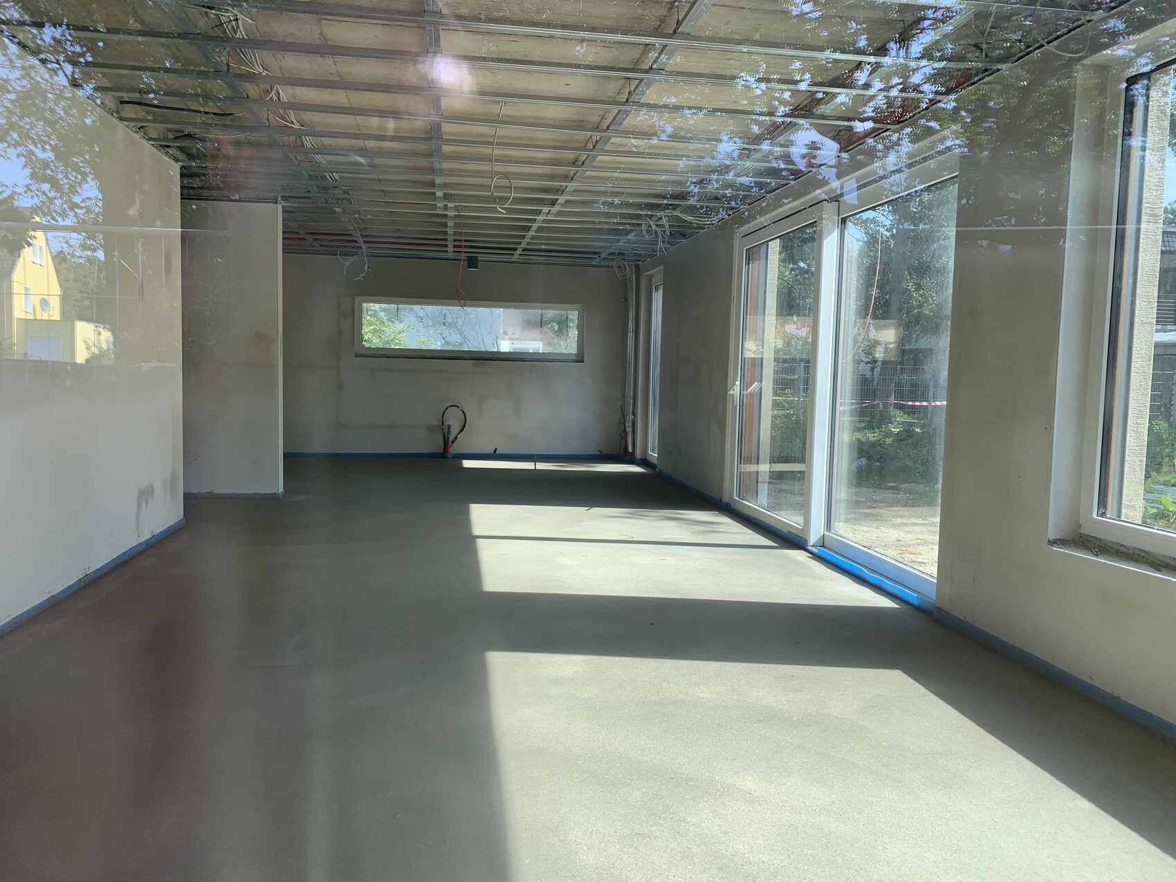 Leerraum unter Bau mit großen Fensterfronten, offener Decke, Kabeln und Betonboden.