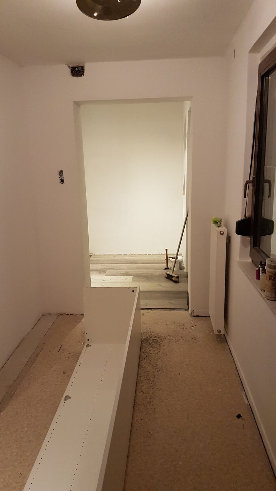 Heller Renovierungsraum mit weißem Schrankaufbau auf dem Boden, Bauwerkzeuge am Fenster.