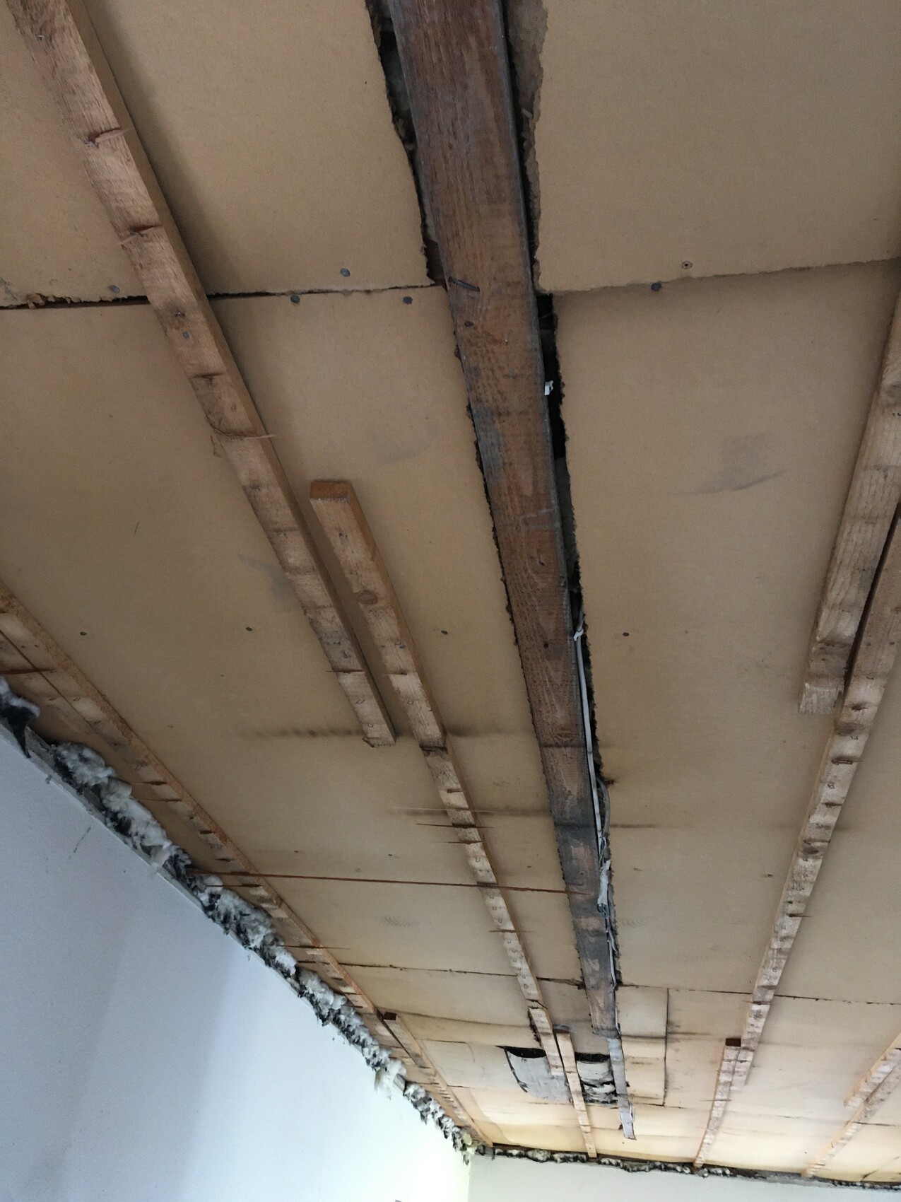 Unterseite einer Decke mit Holzbalken, Dämmplatten, offenem Spalt und Baumaterialresten.