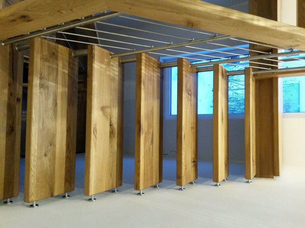 Mehrere vertikale Holzpaneele bilden Raumteiler in einem Innenraum, mit Metallträgern darüber.