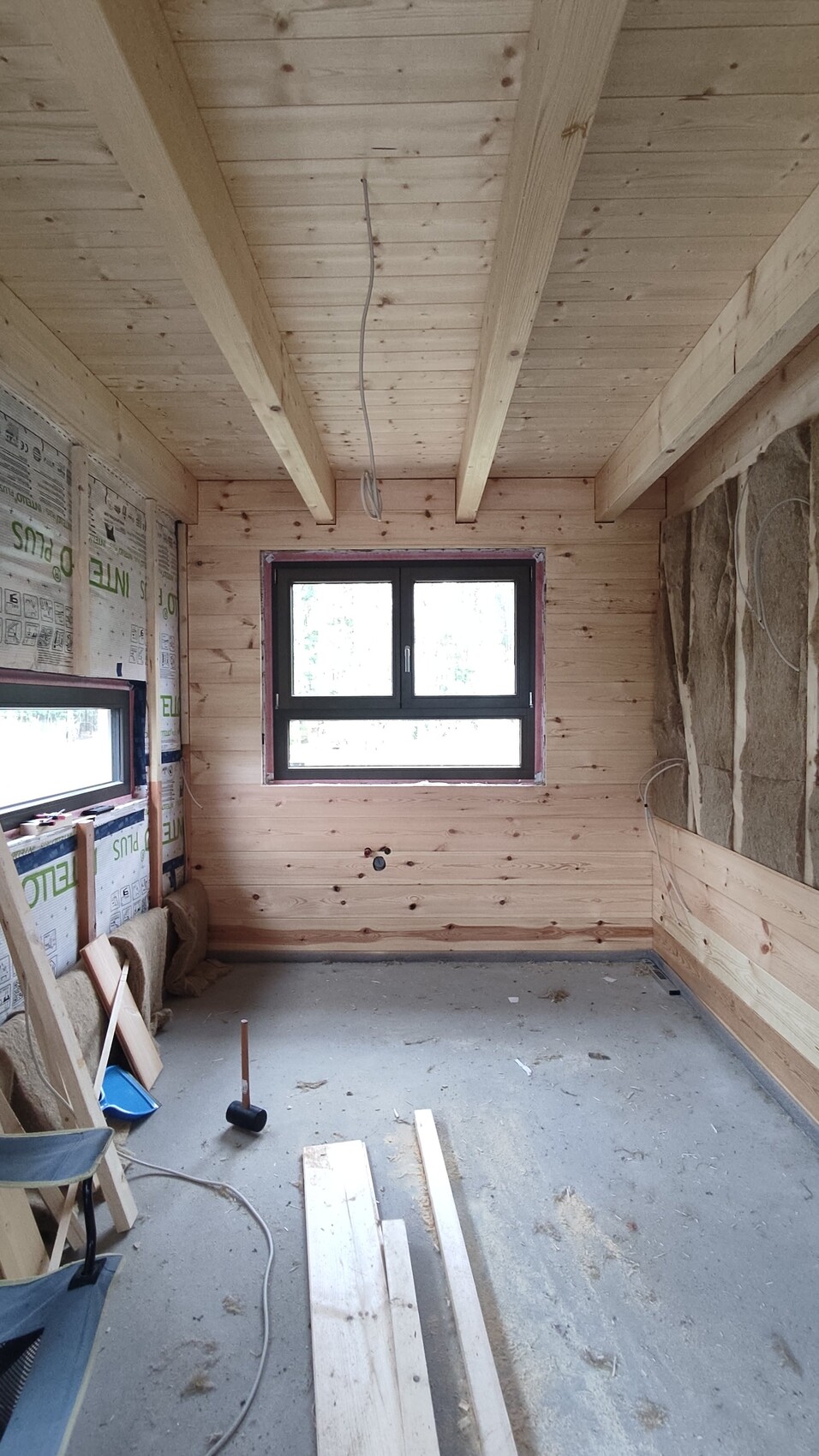Rohbauzimmer mit Holzverkleidung, Deckenbalken, Fenster, Bauholz und Werkzeug auf dem Boden