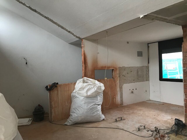 Baustelle im Innenbereich eines Hauses mit Rohbauwänden, Kabeln und Bauabfall.