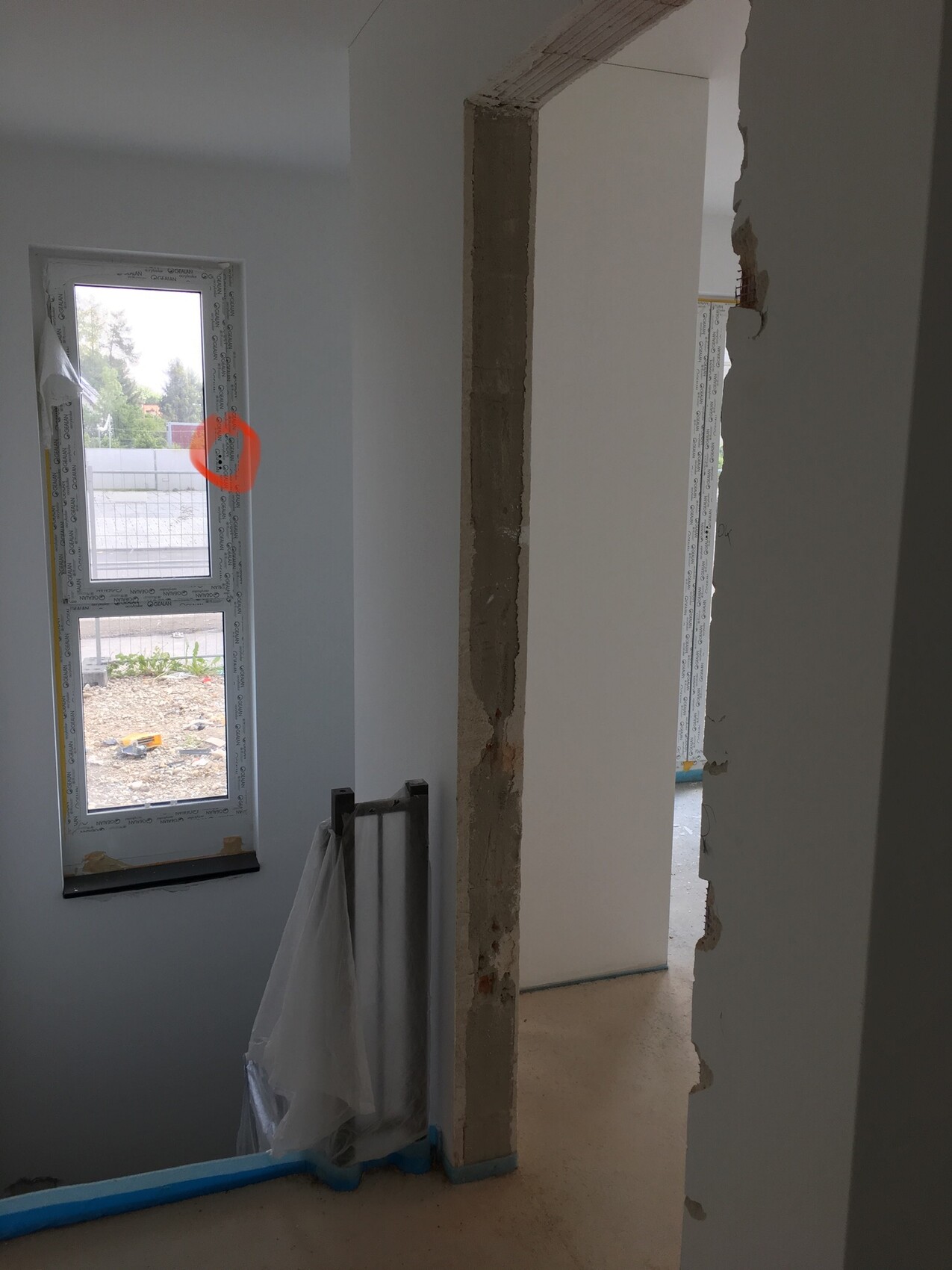 Innenraum einer Baustelle: offener Wanddurchbruch, Fenster mit Folie, abgedeckter Heizkörper.