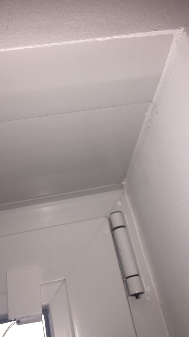Weißer Innenraum im Umbau mit Wand- und Deckenpaneelen, Türrahmen sichtbar.