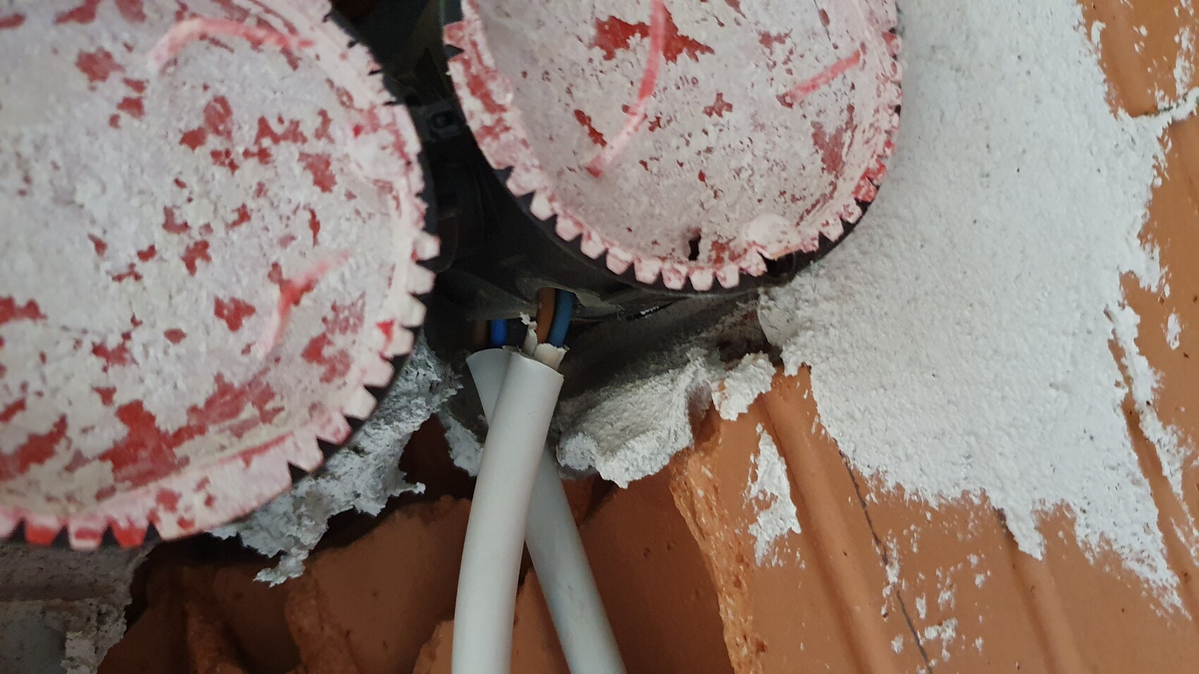 Zwei rote Kreissägeblätter mit Staub bedeckt, darunter blaue Kabel sichtbar.