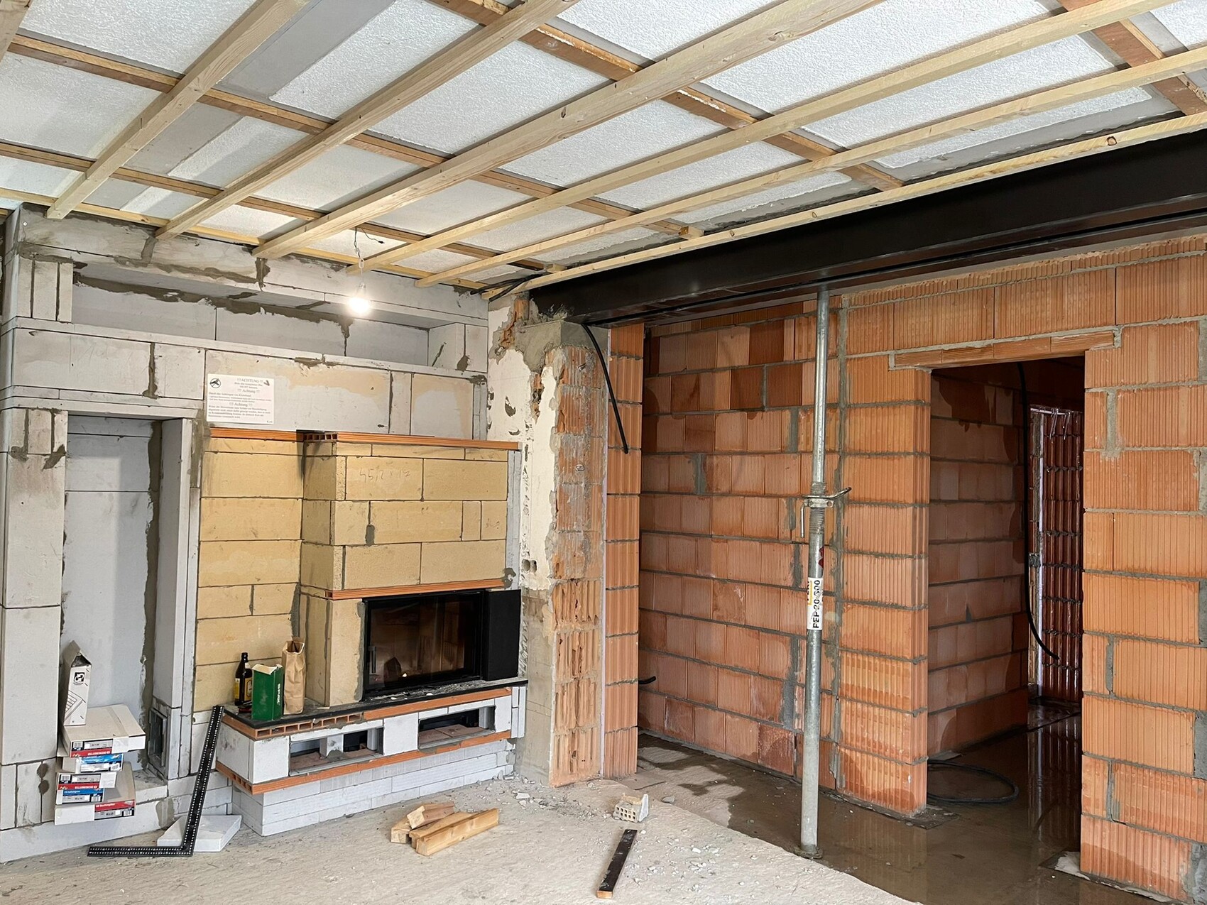 Unfertiger Innenraum mit Kamin aus Stein, Ziegelwänden und Holzdecken-Rahmen
