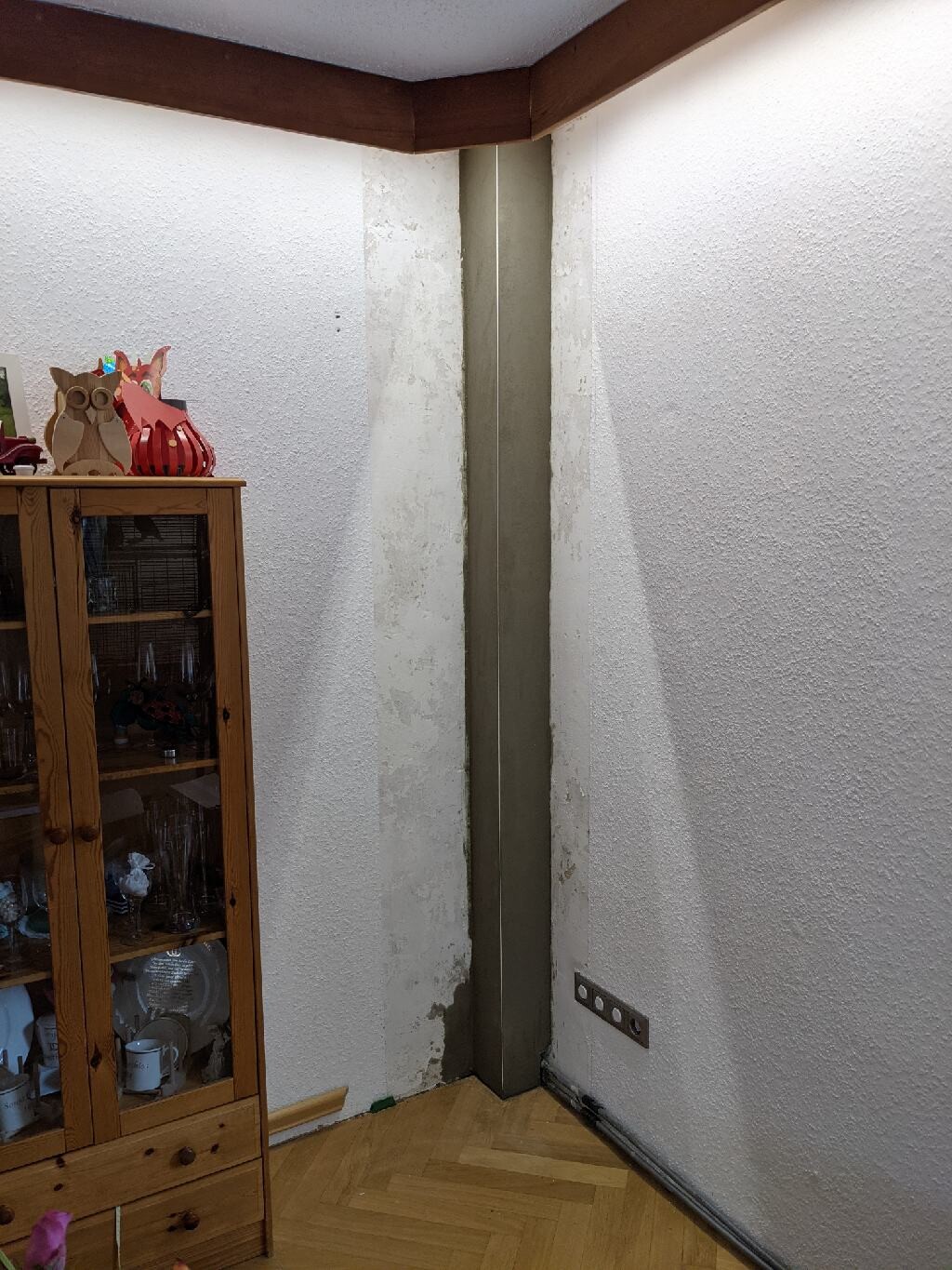 Ecke mit Metallstütze, links Glasvitrine mit Geschirr, Holzboden.