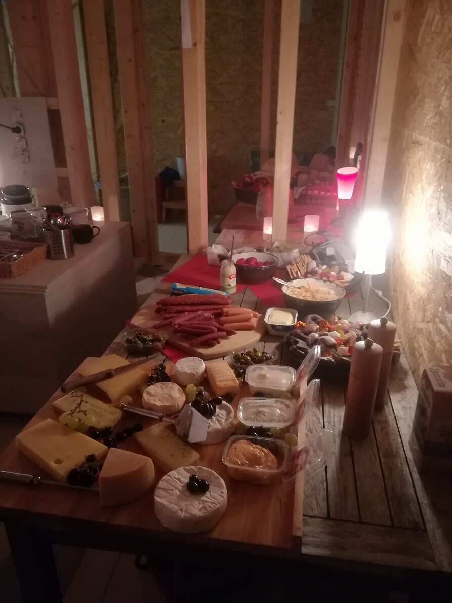 Buffet auf Holztisch mit Käse, Wurst, Oliven, Dips und Brot in warmer Beleuchtung.