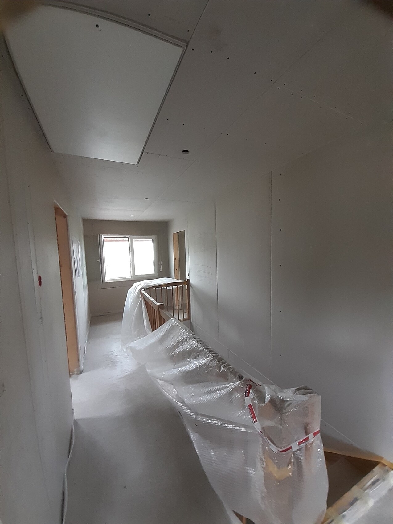 Heller Flur im Bauzustand, Wände/Deckenplatten, Treppengeländer mit Plastikfolie bedeckt.