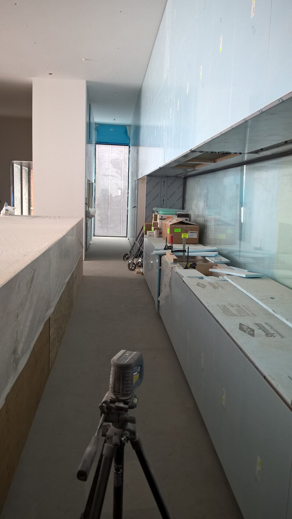 Baustelle eines Innenausbaus: Stativ vorne, linke Arbeitsfläche, blaue Wandverkleidung rechts.