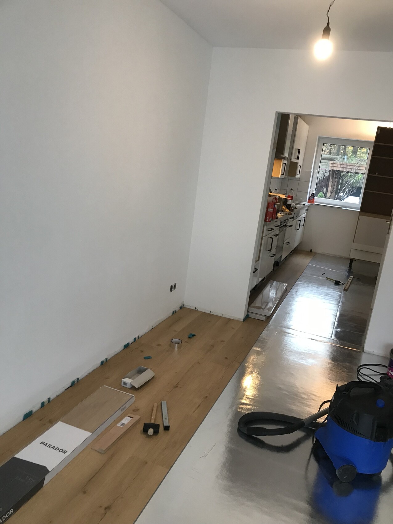 Küche in Renovierung: Holzboden wird verlegt, Werkzeuge und Staubsauger liegen bereit.