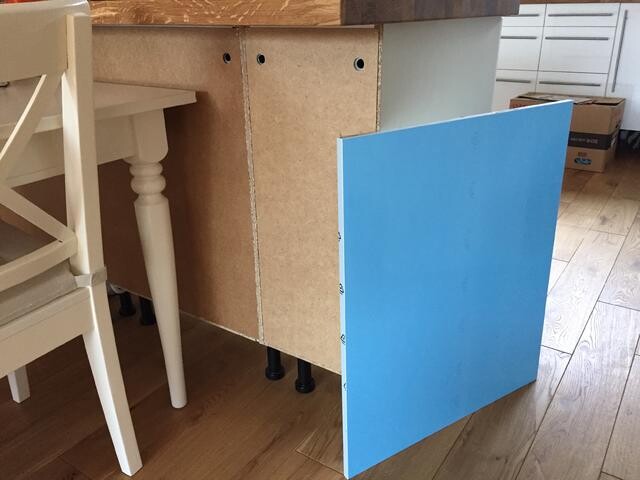 Unterbau eines Küchenunterschranks mit blauer Seitenplatte auf Holzfußboden.