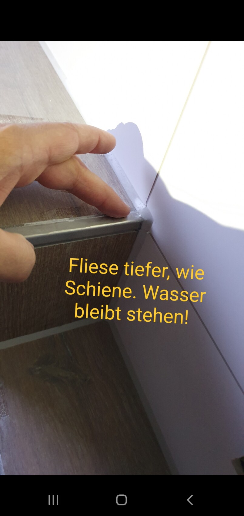 Nahaufnahme: Finger an der Kante eines Holzschranks mit Metallführung, heller Hintergrund.