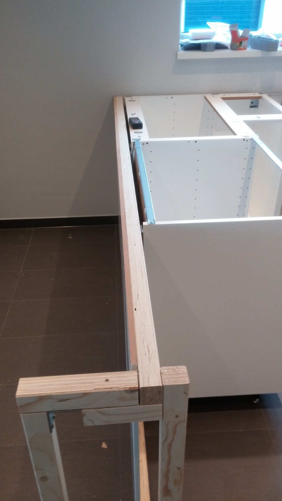 Unvollendete Küchenmöbel-Montage: Holzrahmen, weiße Schränke, Schubladenauszüge, Werkzeuge