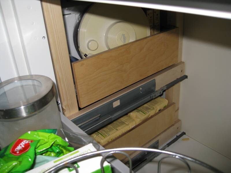 Küchenschrank mit Holzauszügen, sichtbare Schubladenauszüge und Verpackungsmaterial im Vordergrund.