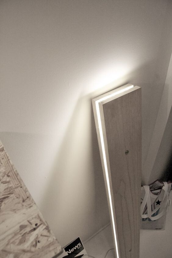 Holzbrett lehnt an der Wand; LED-Lichtleiste läuft entlang der Kante und leuchtet Wand aus.