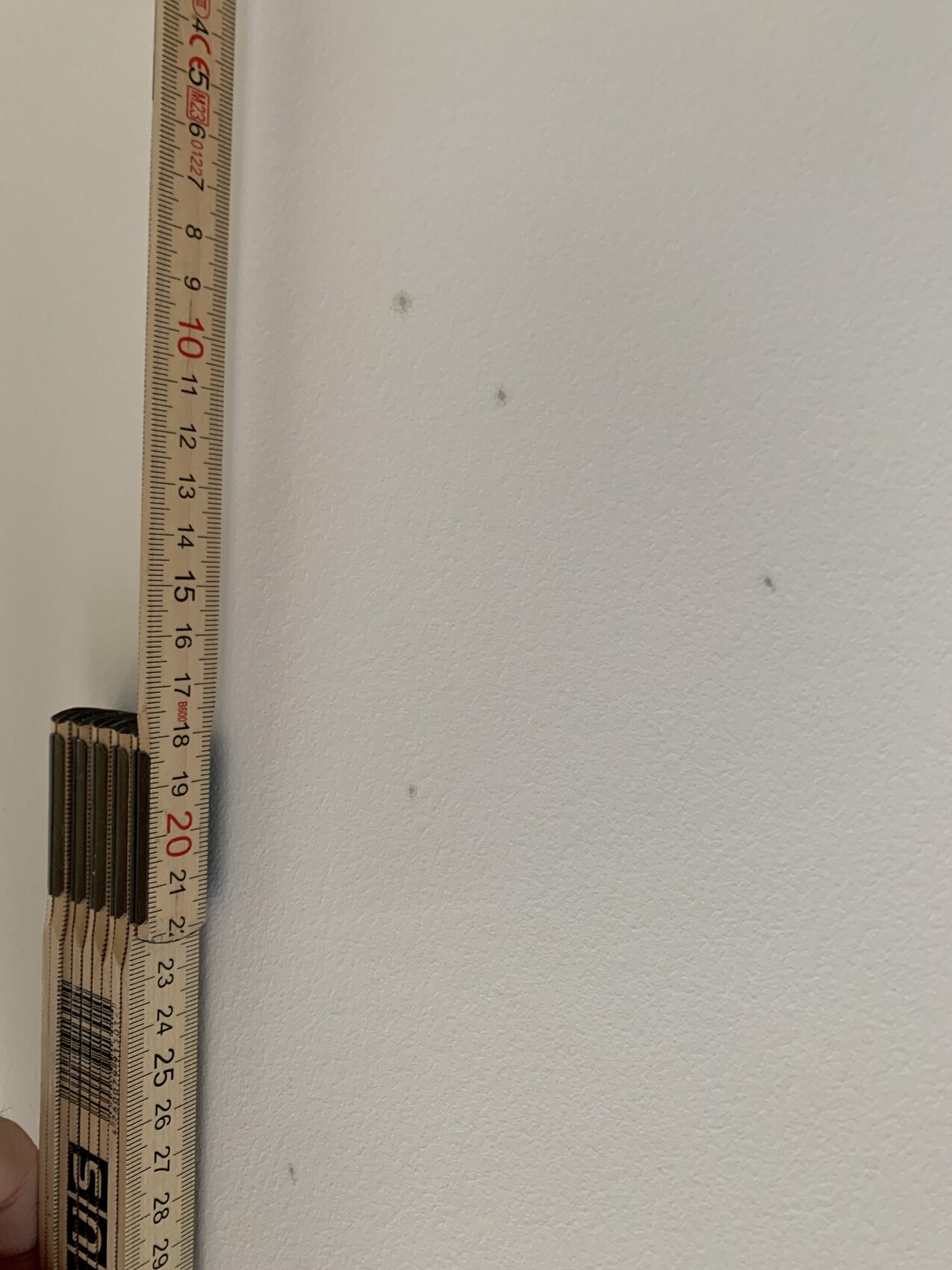Maßband an weißer Wand während Innenausbau, kleine Flecken sichtbar.
