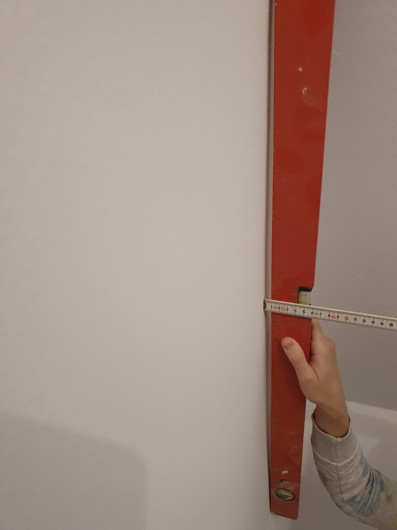 Hand misst mit Massband an rotem Stahltraeger in Innenraum