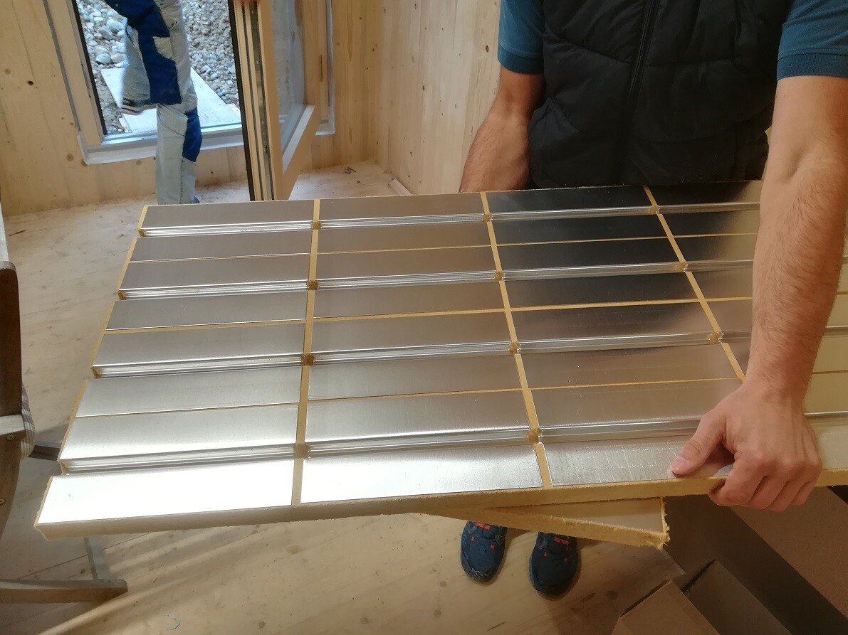 Person hält eine Platte aus silbernen Metallfliesen mit goldenen Fugen in einer Bauwerkstatt.