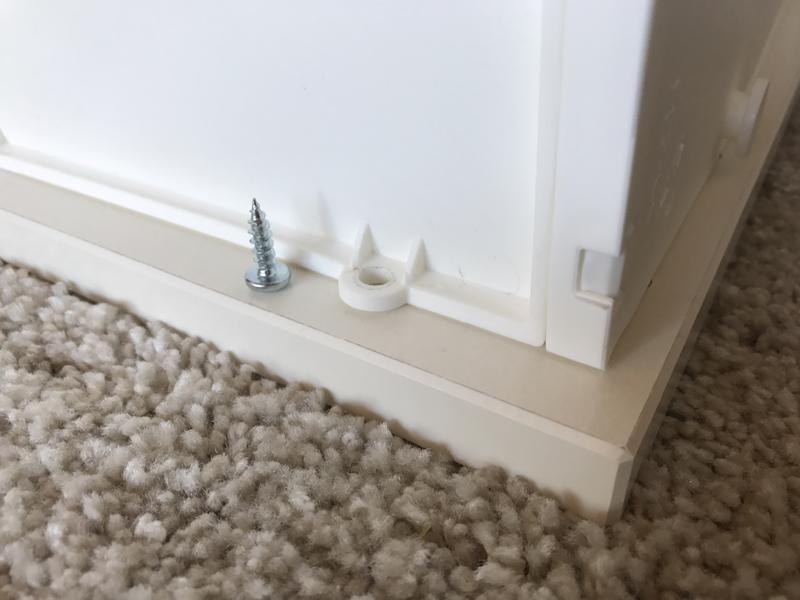 Unterseite eines weißen Möbelstücks auf Teppich; Schraube und Kunststoffabstandhalter sichtbar.