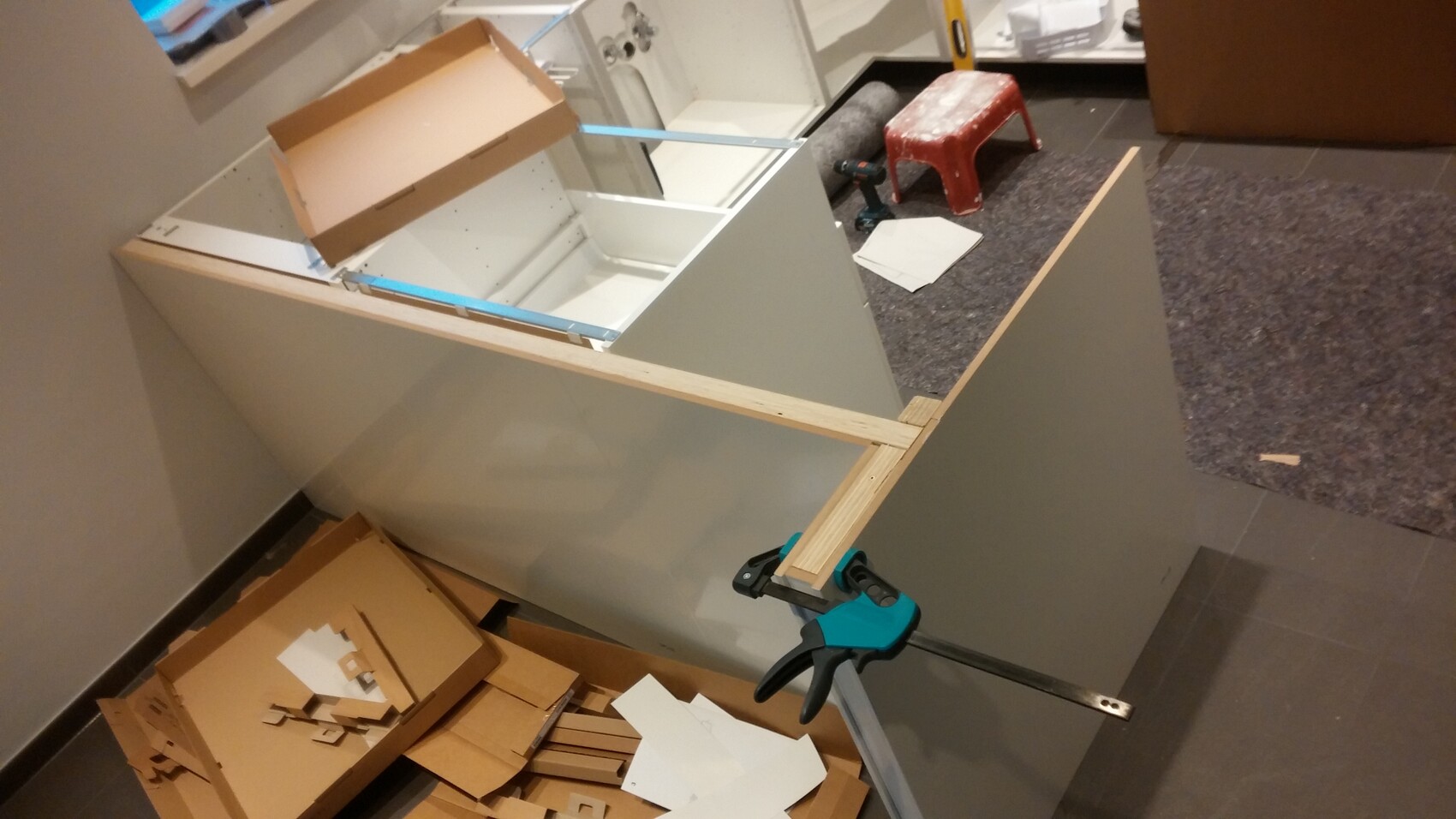 Möbelbau: Holzrahmen und Platten auf einer Werkbank, blaue Zwinge klemmt das Teil fest.