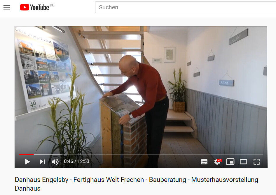 Mann im roten Pullover begutachtet ein Backstein-Display im Musterhaus-Showroom neben einer Treppe.