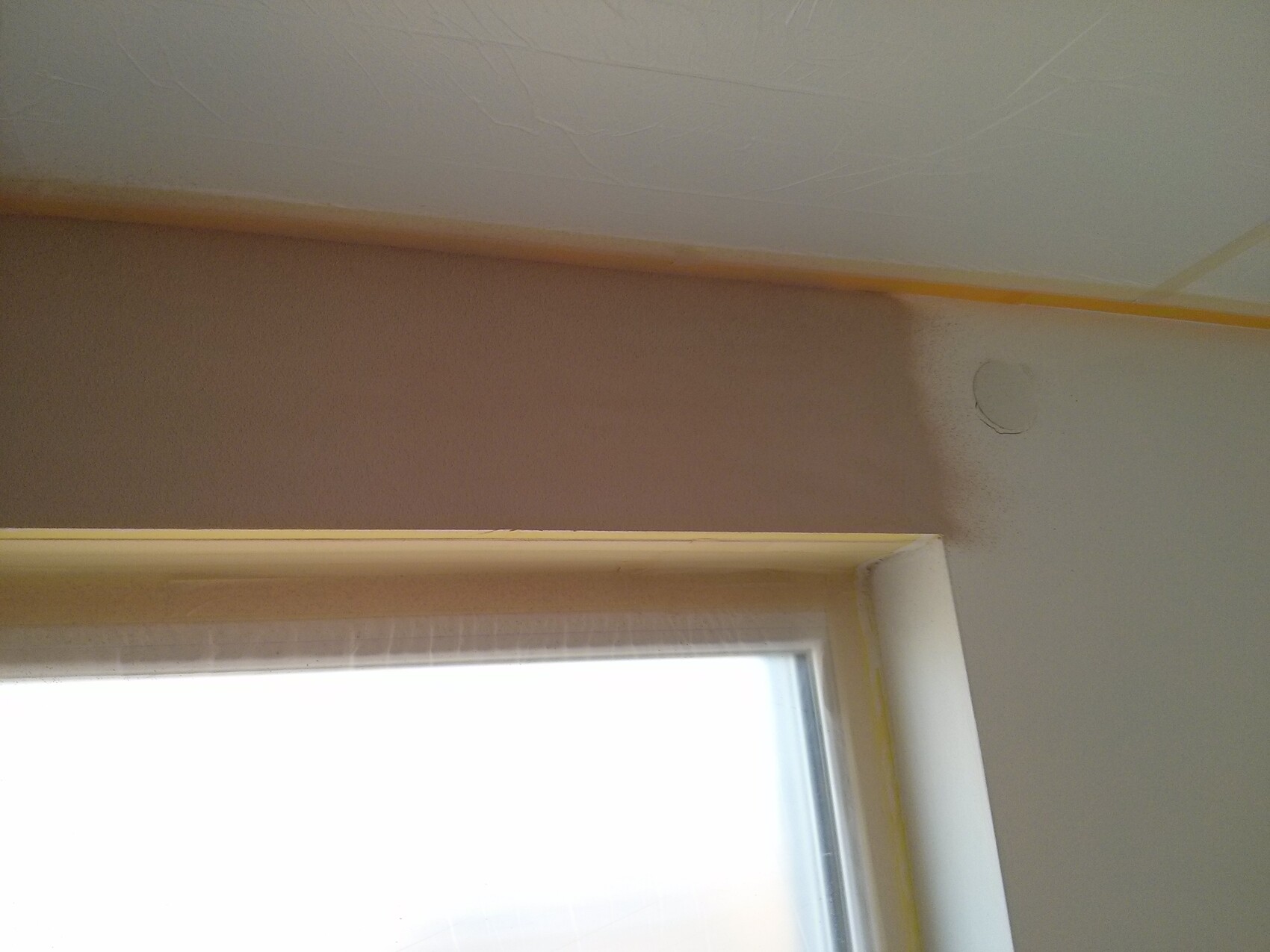 Innenraum mit Fenster unten; brauner Wandstreifen und runde Reparaturstelle; Malerkrepp an Deckenrand.