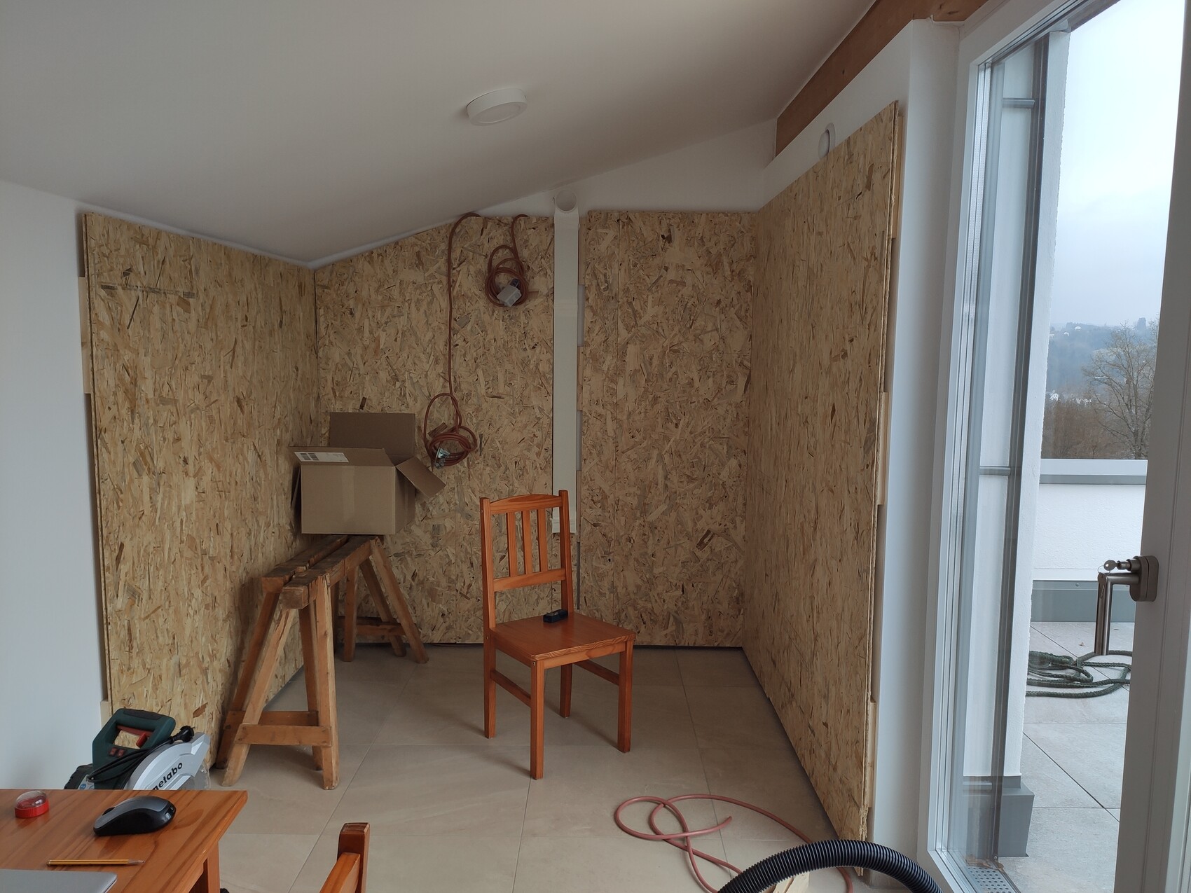 Renovierungsraum mit OSB-Wänden, Bauwerkzeugen, Holzbalken und Balkonzugang