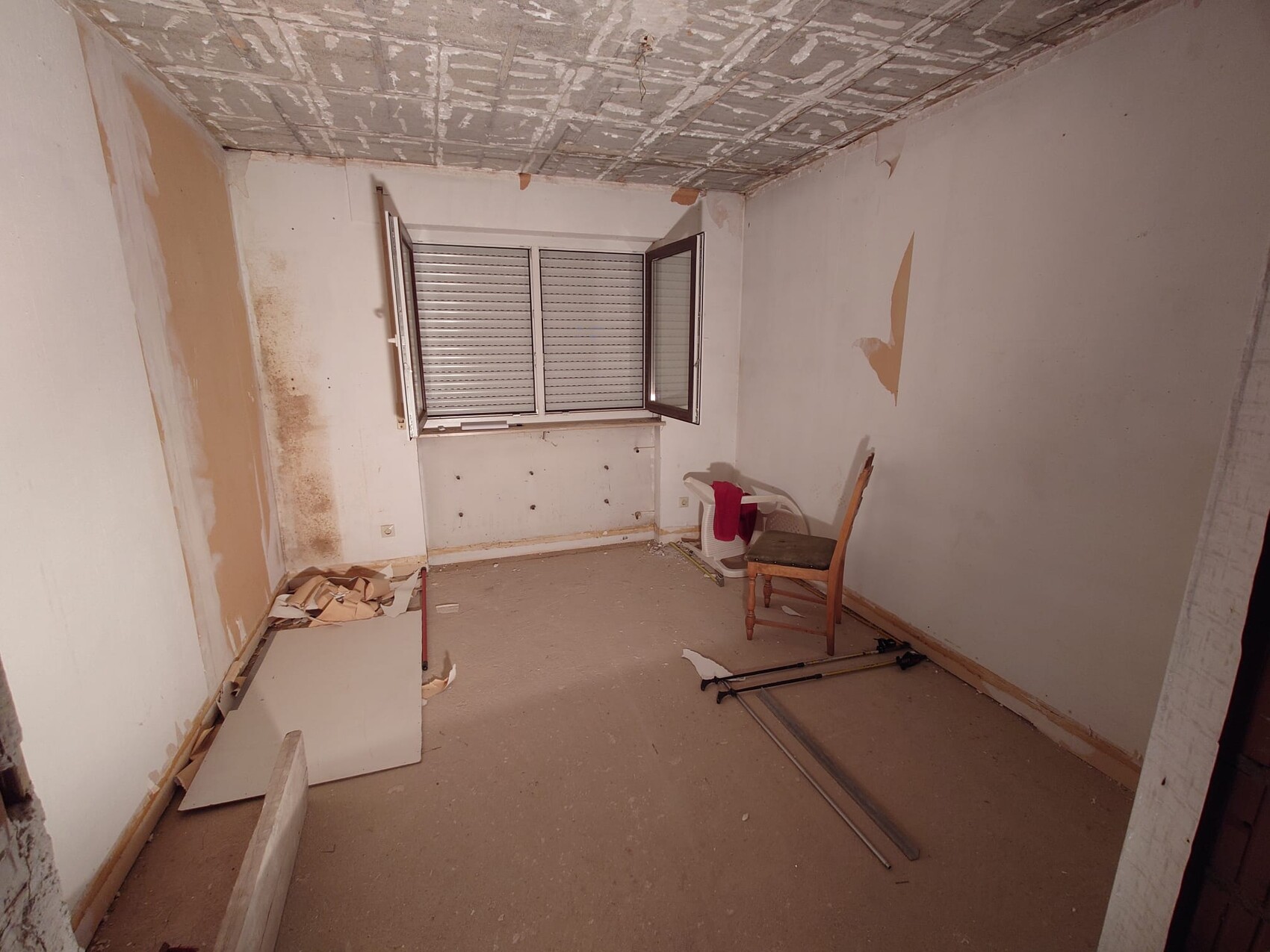 Leerer Innenraum in Renovierung mit offener Decke, Fenster, Möbelresten und Baumaterialien