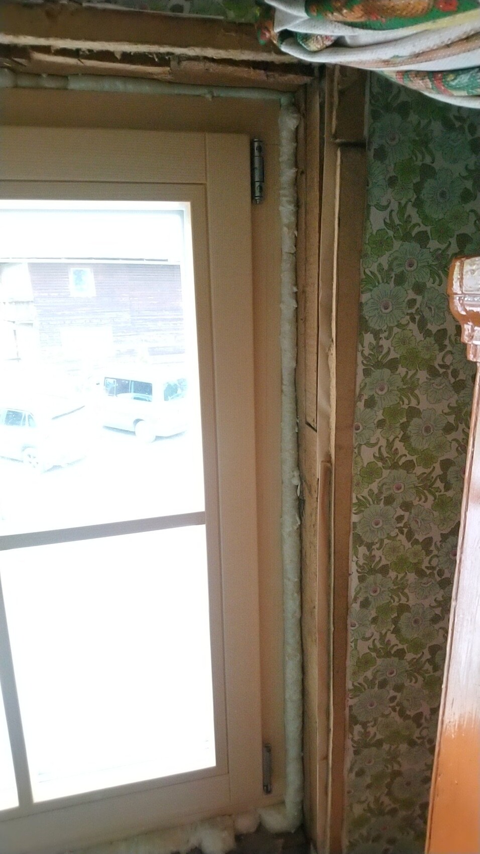 Fensterrahmen in Renovierungsbereich; freigelegte Wand, Isolierrohr, grüne Tapete.