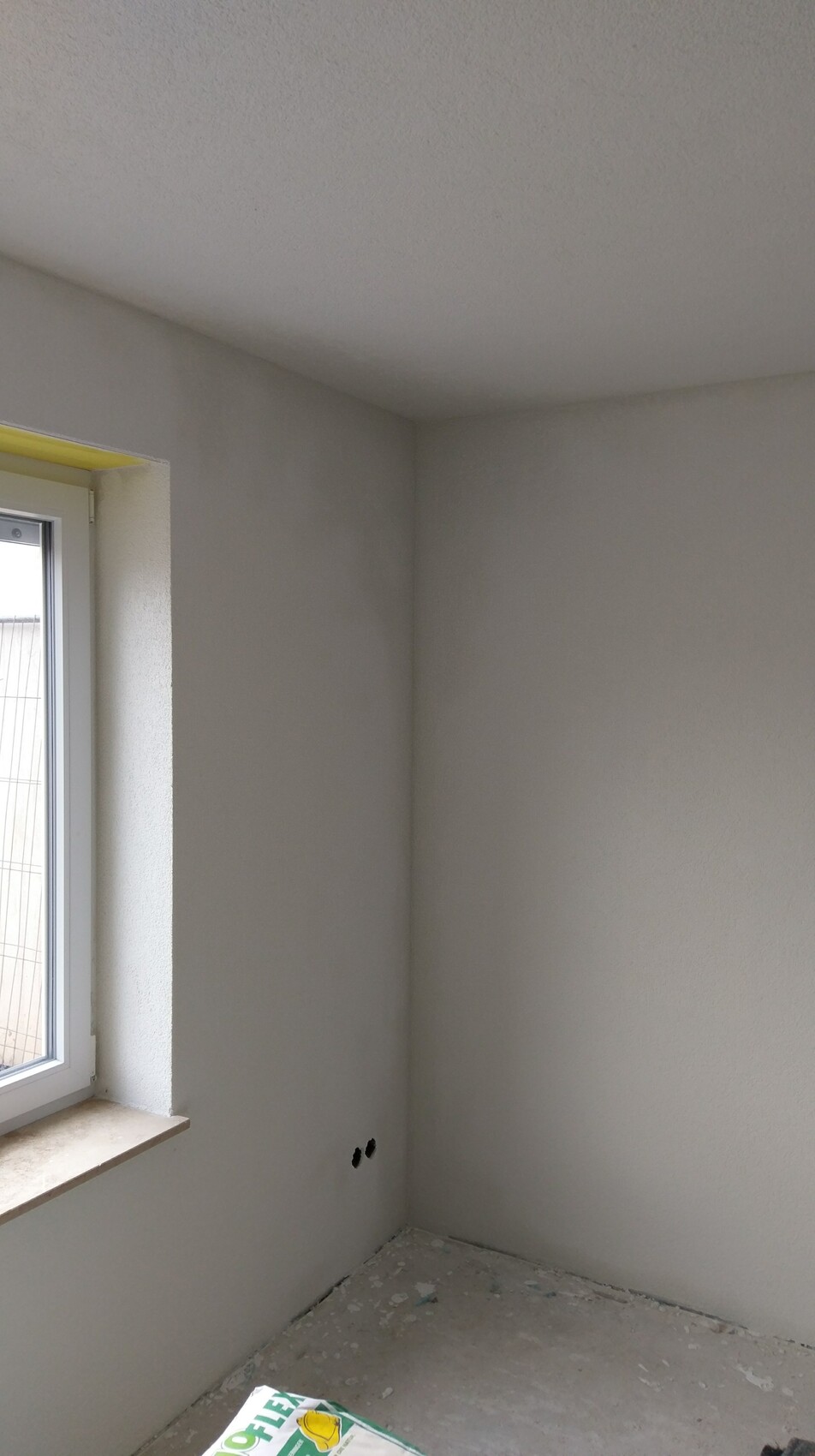 Innenraum im Bauzustand: verputzte Wände, Fensterfront, Boden mit Bauabfällen