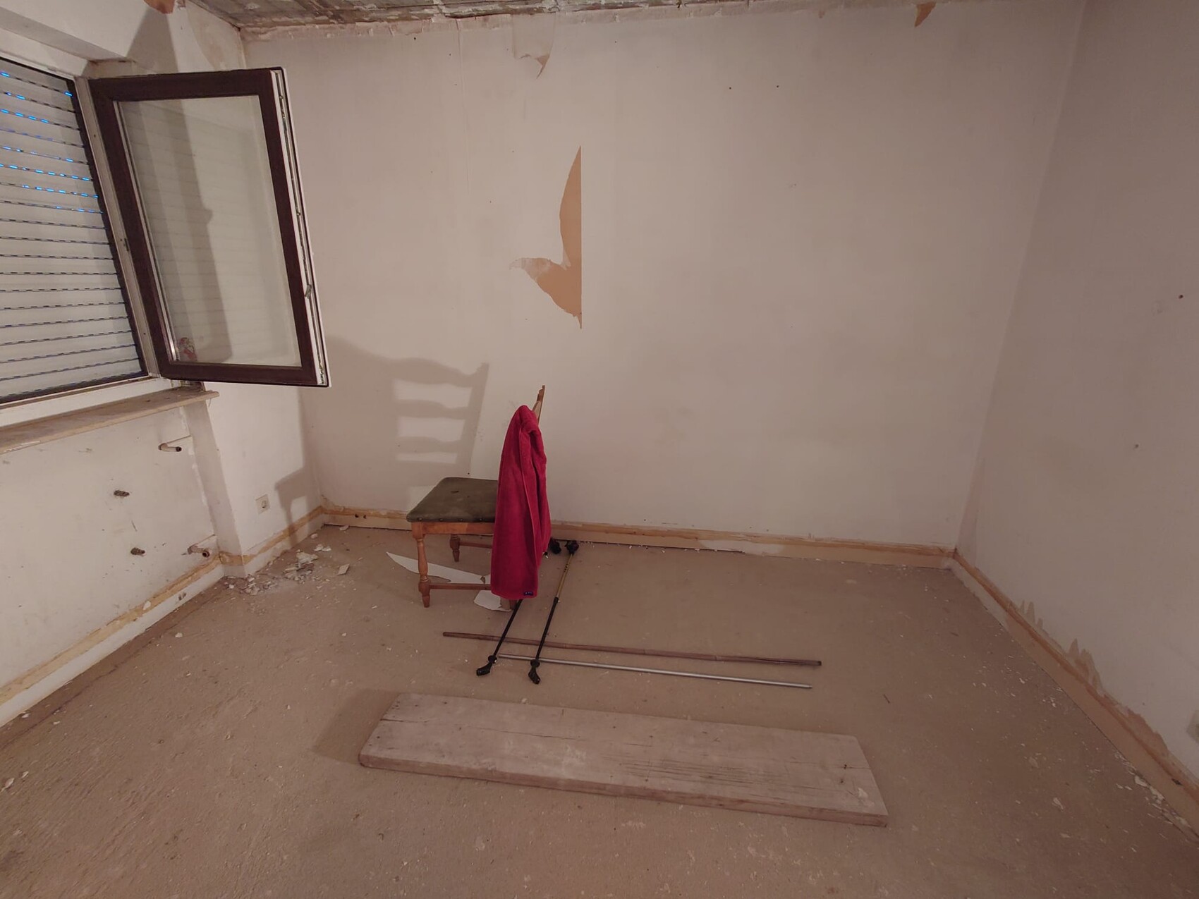 Leerer Renovierungsraum mit offener Fensterfront, Wandreparaturstelle und Bauwerkzeugen am Boden.