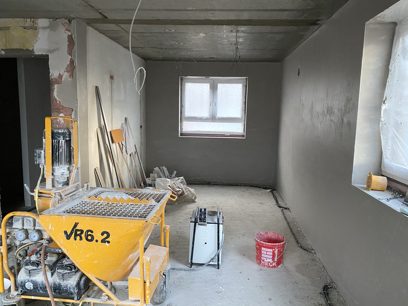 Unfertiger Baustellenraum mit gelbem Betonmischer VR6.2, Werkzeugen und rotem Eimer.