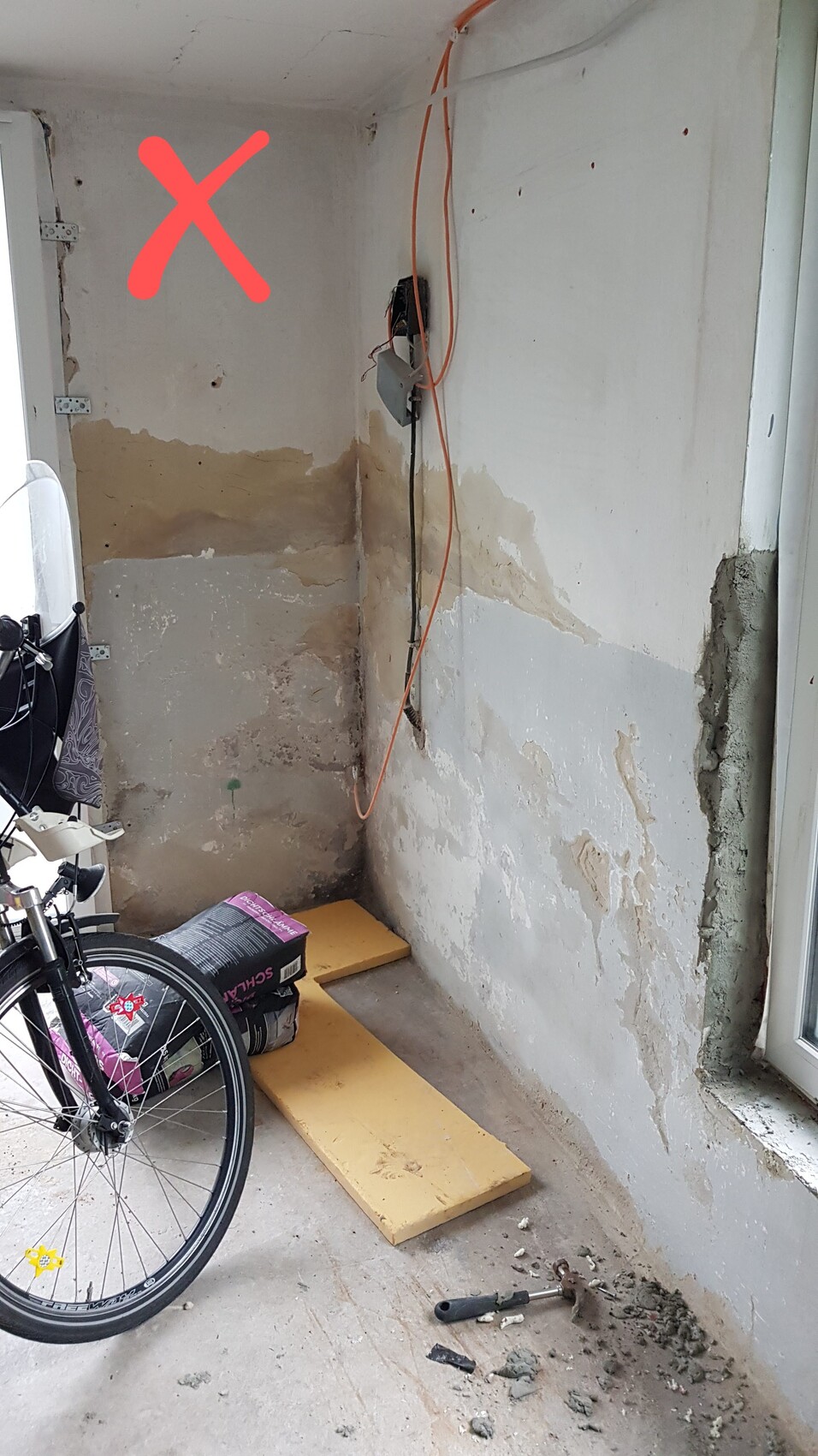 Renovierungsbereich im Innenraum mit freiliegenden Leitungen, Bauabfällen und rotem X.